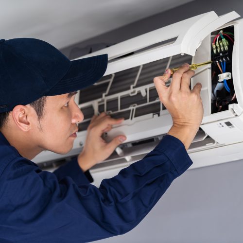 Electrician with screwdriver repairing the air conditioner indoors